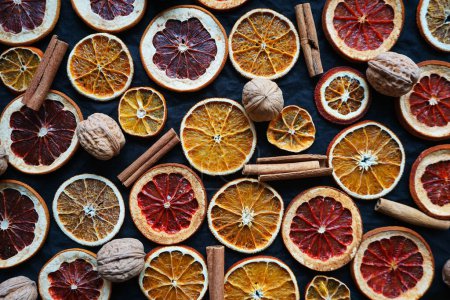 Photo for Dry orange and grapefruit slices next to cinnamon and walnuts on a dark background - Royalty Free Image