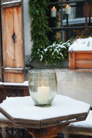 Téléchargez les photos : Une bougie allumée dans un chandelier en verre sur une table en bois à l'extérieur sur fond d'arbre de Noël - en image libre de droit