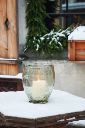 Téléchargez les photos : Une bougie allumée dans un chandelier en verre sur une table en bois à l'extérieur sur fond d'arbre de Noël - en image libre de droit