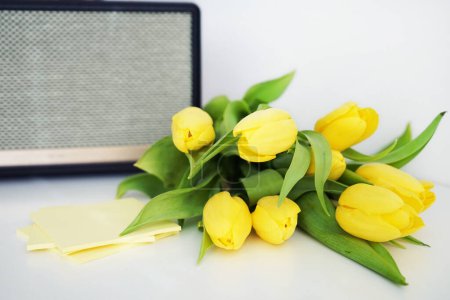 Yellow tulips next to yellow stickers against the background of a music speaker