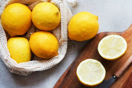 Whole lemons next to cut ones on a wooden board next to a knife on a light background