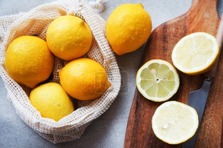 Whole lemons next to cut ones on a wooden board next to a knife on a light background