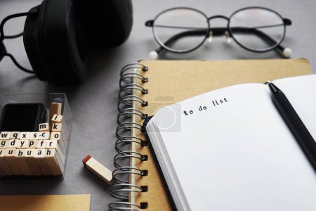 Bloc de notas junto a bolígrafo, notas adhesivas, gafas, smartphone y auriculares sobre fondo gris