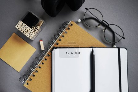 Notizblöcke neben Stift, Notizen, Brille, Smartphone und Kopfhörer auf grauem Hintergrund
