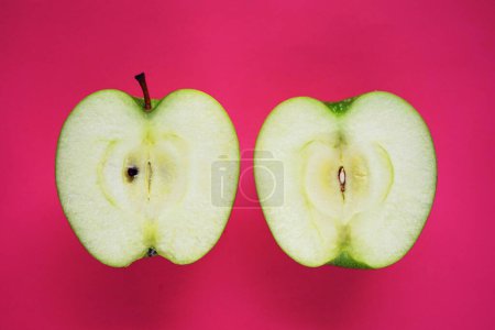 Téléchargez les photos : Moitiés d'une pomme verte mûre sur fond rose - en image libre de droit