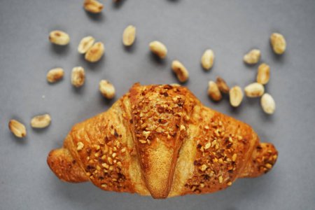 Croissant with peanut crumbs and cream next to scattered peanuts