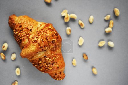 Croissant with peanut crumbs and cream next to scattered peanuts