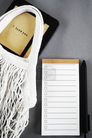 To-do-Liste neben Notizblock, Haftnotiz und Einkaufstasche auf grauem Hintergrund