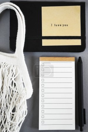 Lista de tareas pendientes junto al bloc de notas, la nota adhesiva y la bolsa de compras sobre fondo gris