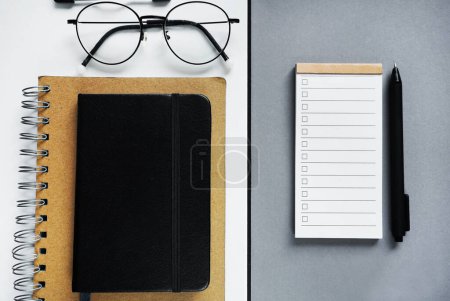 Bloc de notas con lista de tareas al lado de bloc de notas, bolígrafo, gafas sobre fondo gris