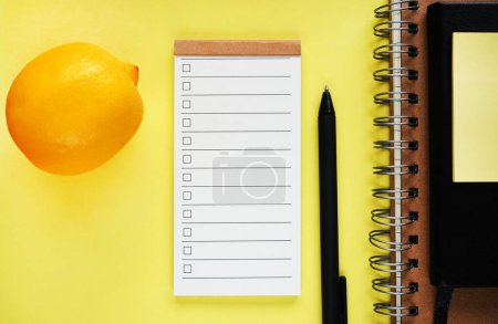 To-do-Liste neben Zitrone, Notizblock und Stift auf gelbem Hintergrund