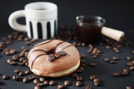 Photo for Caramel donut with coffee decor next to a cup with black coffee and a glass ladle with coffee on a dark background - Royalty Free Image