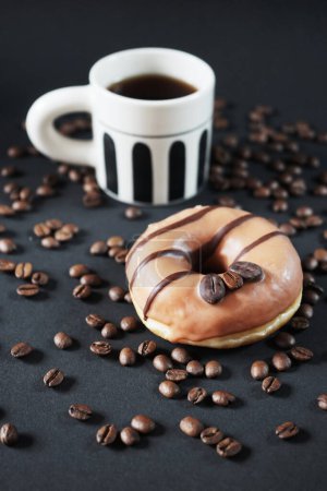 Foto de Donut de caramelo con decoración de café junto a una taza de café negro sobre un fondo oscuro - Imagen libre de derechos