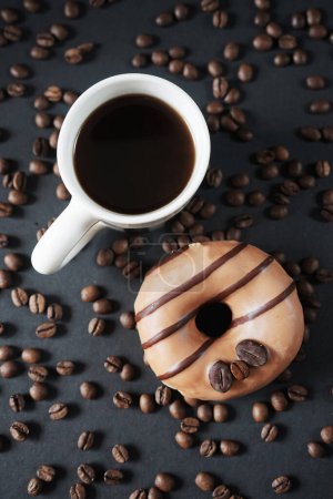 Photo for Caramel donut with coffee decoration next to a cup of black coffee on a dark background - Royalty Free Image