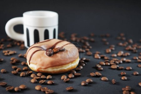 Foto de Donut de caramelo con decoración de café junto a una taza de café negro sobre un fondo oscuro - Imagen libre de derechos