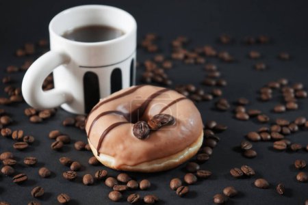Photo for Caramel donut with coffee decoration next to a cup of black coffee on a dark background - Royalty Free Image