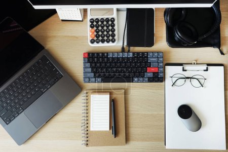 Desktop with notepads, laptop, monitor, keyboard, mouse, headphones on a light background