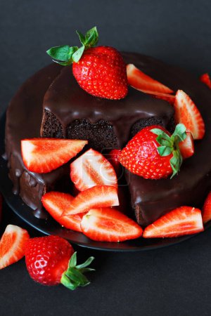 Chocolate cake with chocolate icing and fresh strawberries on a dark background