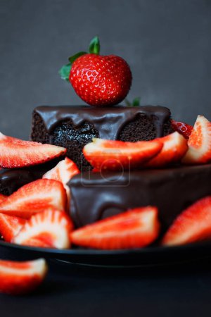 Pastel de chocolate con glaseado de chocolate y fresas frescas sobre un fondo oscuro