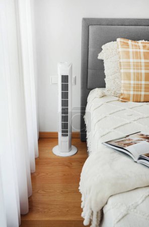 White tower fan next to the bed in a modern bright bedroom