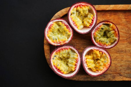 Passion fruits cut in half on a wooden tray on a dark background