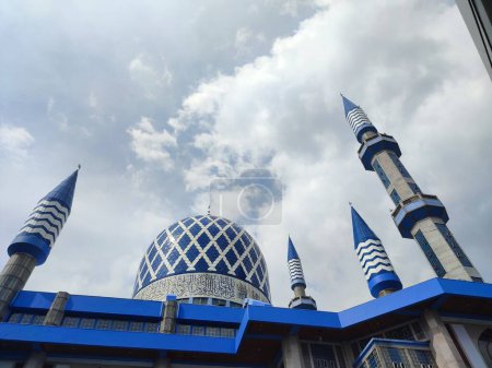 The blue dome of the mosque has a background of sky and clouds
