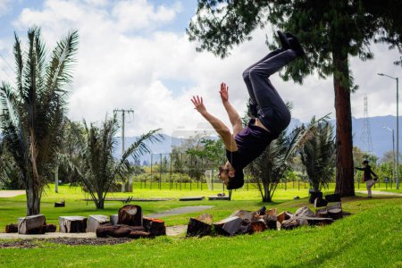 Photo for Young man doing a back flip in a park, practicing gymnastics outdoors - Royalty Free Image