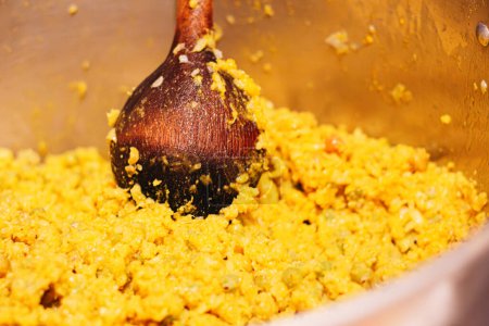 Schöpfkelle rührt gelben Teig mit Zutaten für eine kolumbianische Tamale in einer Küche kochen