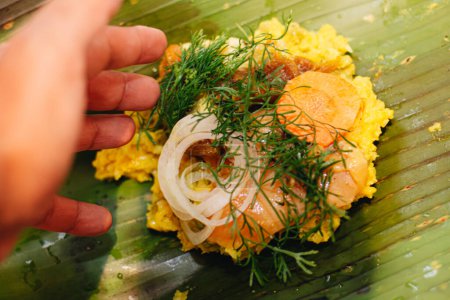 hand of an elderly woman preparing the ingredients of a Colombian tamale on some banana leaves