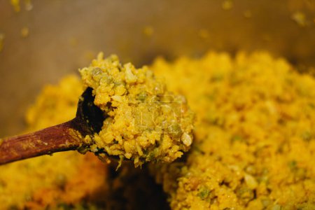 Schöpfkelle rührt gelben Teig mit Zutaten für eine kolumbianische Tamale in einer Küche kochen