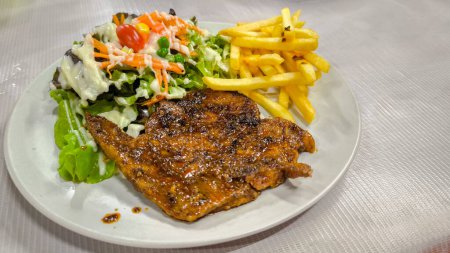 Bifteck de porc Mala épicé, longe de porc, épaule de porc, sauce épicée bien cuite. salade accompagnées de légumes crus, chêne vert, maïs avec vinaigrette crémeuse et frites locales