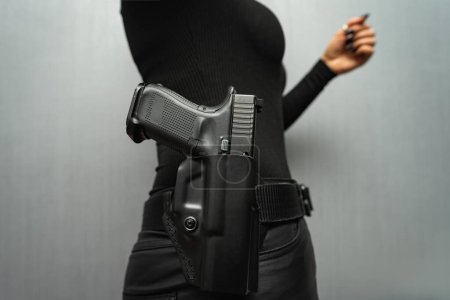 A pistol in a holster in a girl on a black jeans belt.