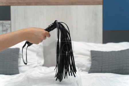 Whip in a woman's hand on the background of the bed. High quality photo