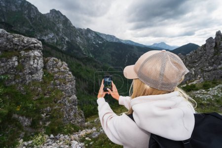 A girl takes a photo with her phone high in the Tatra mountains, the sky is overcast with storm clouds, photo from the back. High quality photo