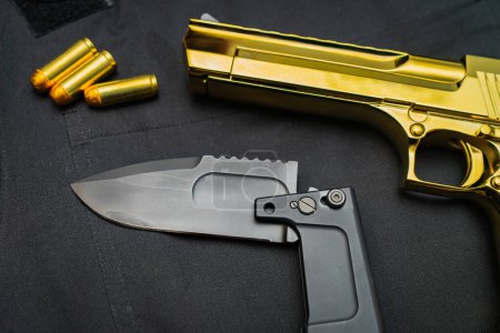Foto de Firearms and bladed weapons. Gold color Desert Eagle pistol and folding tactical knife, close up. - Imagen libre de derechos