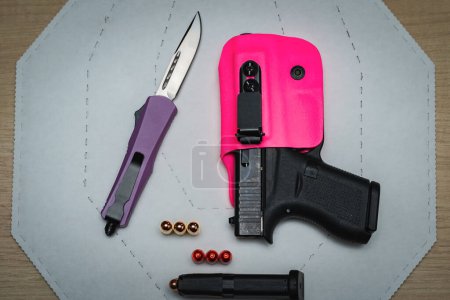 Téléchargez les photos : Weapons for the lady, a pistol in a pink holster, a folding knife with a purple handle and cartridges. High quality photo - en image libre de droit