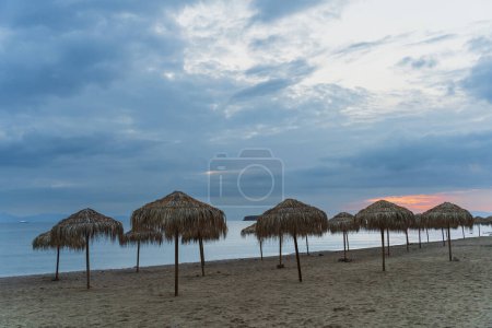 Photo for Greek beach with palm umbrellas in Varkiza in the off season at sunset. High quality photo - Royalty Free Image