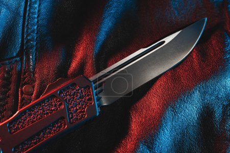 Close-up photo of a automatic folding sharp knife on a leather jacket. High quality photo