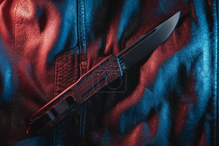 Close-up photo of a automatic folding knife on a leather jacket. High quality photo