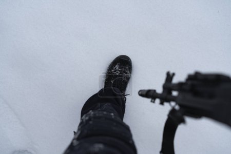 Der Fuß eines Soldaten in einem taktischen Stiefel und mit einem Gewehr vor dem Hintergrund des Schnees. 