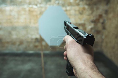 Eine Pistole in der Hand eines Mannes zielt auf eine Papierscheibe auf einem Schießstand. Hochwertiges Foto