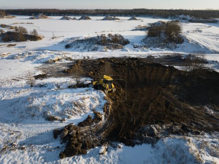 A yellow bulldozer works in a field in winter, air photo from a drone. 