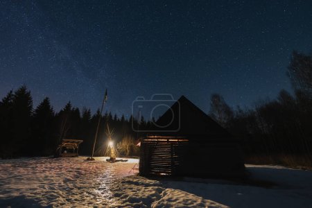 Landscape astrophotography in winter in Estonian farm. A small house in the forest glows in the dark. Kollassaare. 