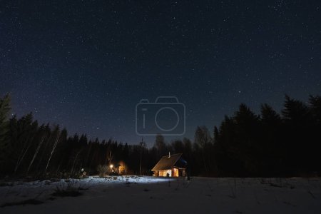 Landscape astrophotography in winter in Estonia. A small house in the forest glows in the dark. Kollassaare. 