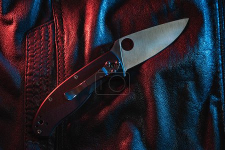 Close-up photo of a pocket folding knife on a leather jacket. 
