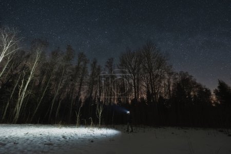 Male traveler with a headlamp in a winter night forest. Landscape astrophotography. 