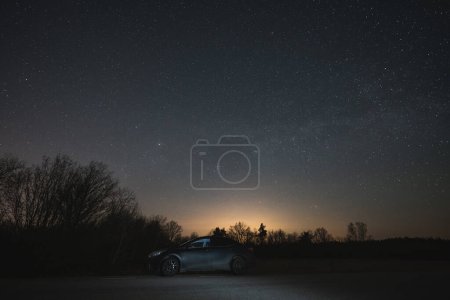 Night scene, a black car parked in nature under the starry sky. 