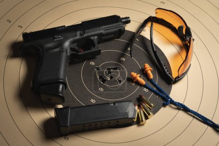 Zielscheibe mit Einschusslöchern in der Mitte, Pistole, Munition, Schutzbrille und Ohrstöpseln. 