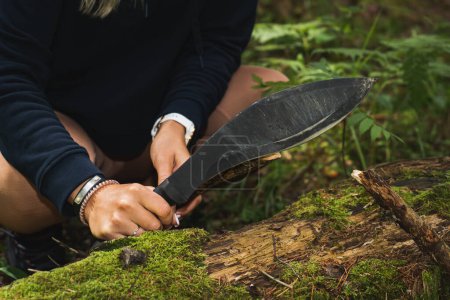 Una niña sostiene una espada kukri en sus manos al aire libre en el bosque para cortar madera. 