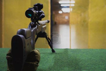 Un rifle de francotirador con mira óptica y un bípode en un campo de tiro. 